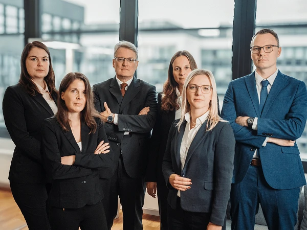 Schick gekleidetes Kanzleiteam vor moderner heller Fensterfront