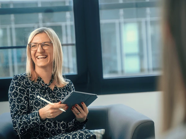 Frau mit iPad lachend auf Sofa im modernen Büro