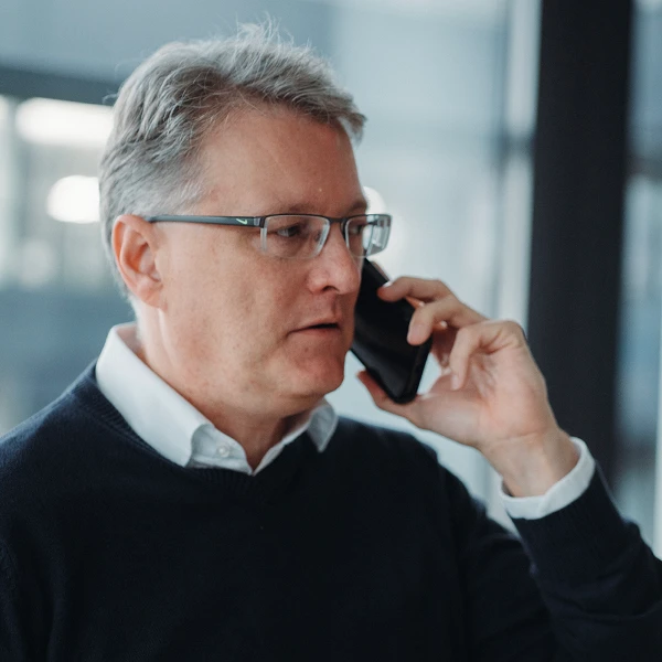 Älterer Mann mit Hemd und Pullover am telefonieren